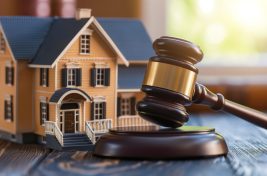 Real Estate Law Concept with Gavel and House Model. A model home next to a judge's gavel on a wooden desk, depicting real estate law, property disputes, and legal proceedings.